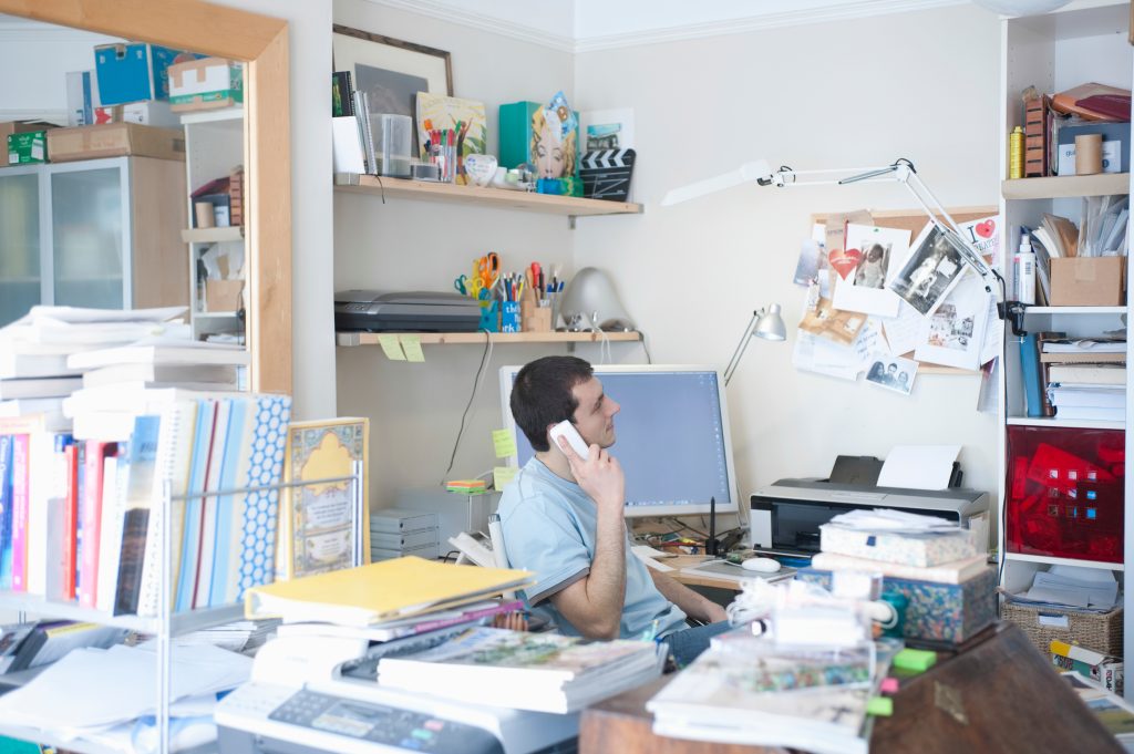 A well ordered home office with a man at a desk on the phone as he works from home.