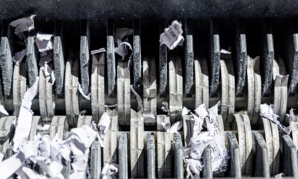 The back of a Paper Document Shredder's cutting teeth showing tiny cross cut pieces of paper and paper documents
